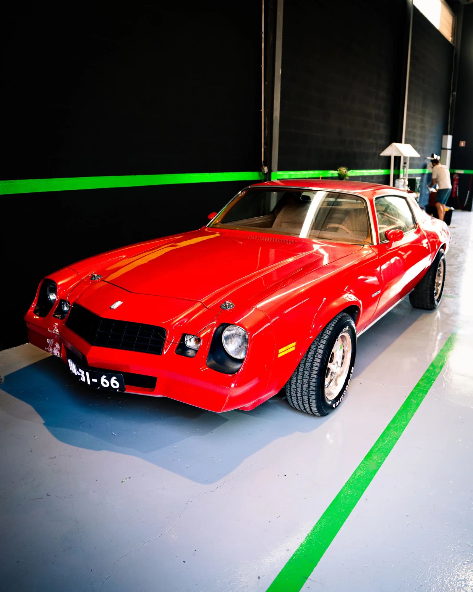 Chevrolet Camaro clássico vermelho na oficina, junto à parede preta com a faixa verde