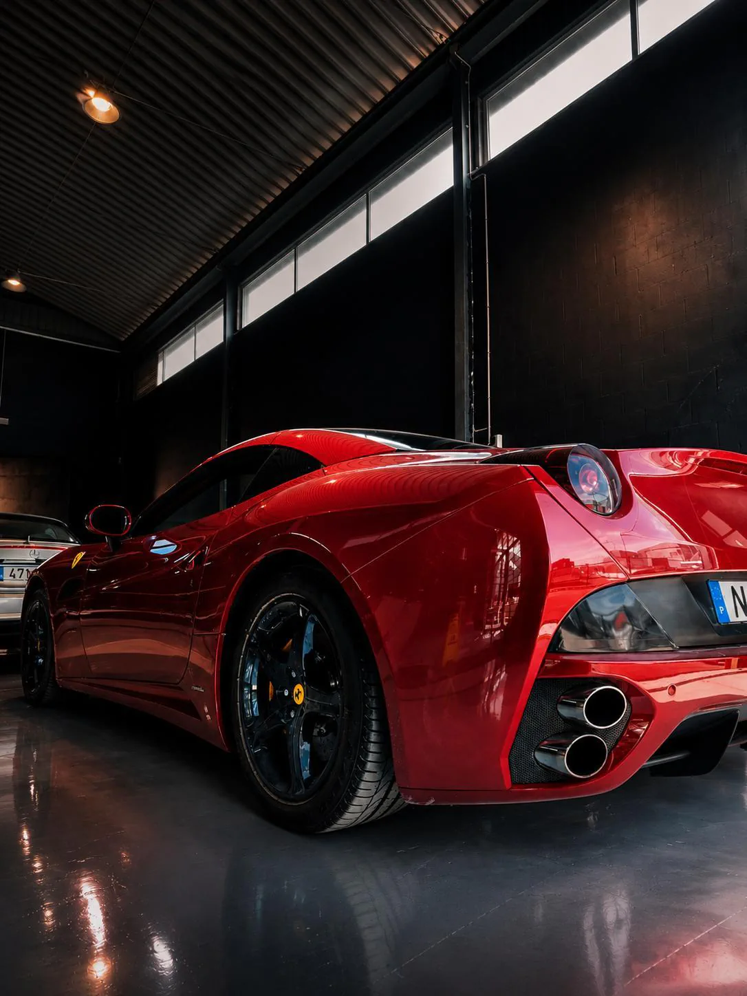 Traseira de um Ferrari California vermelho sob as janelas altas da oficina