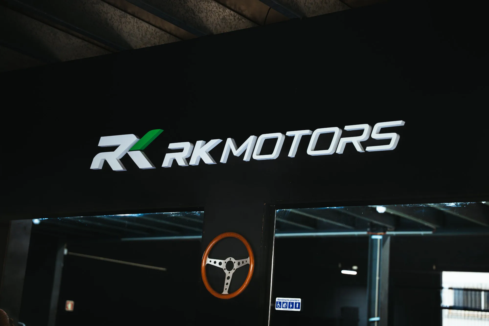 Logótipo da RKMotors em relevo por cima da entrada, com um volante de madeira na parede