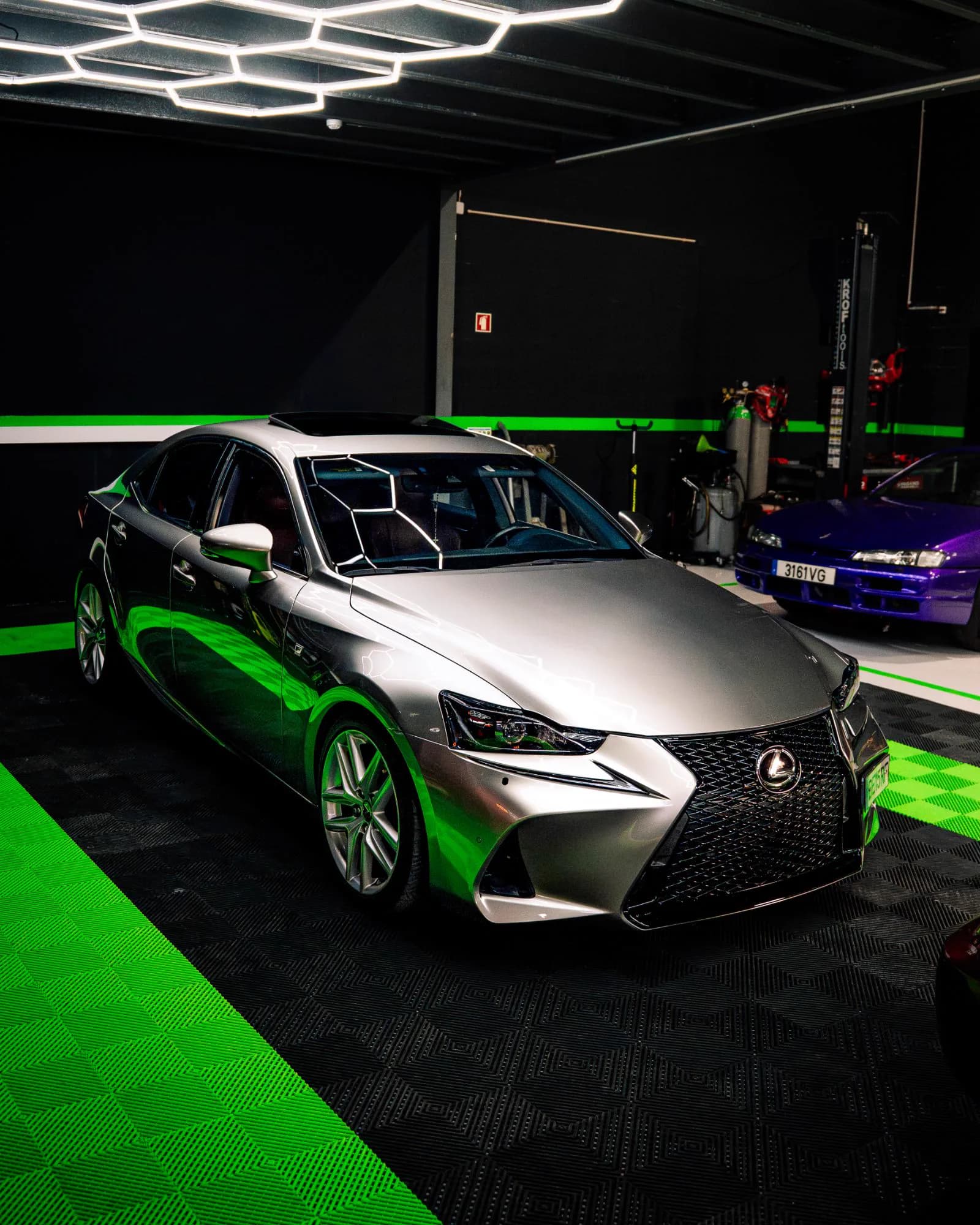 Lexus IS cinzento sob o teto de luzes hexagonais, sobre o piso verde e preto