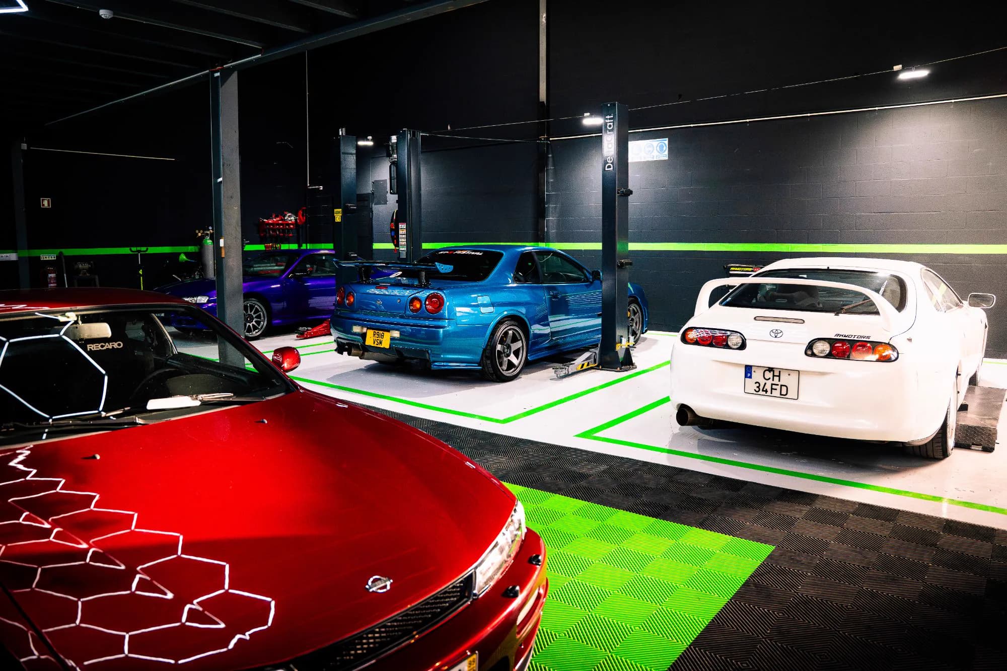 Nissan Silvia S14 vermelho, Skyline R34 azul e Toyota Supra branco alinhados na oficina