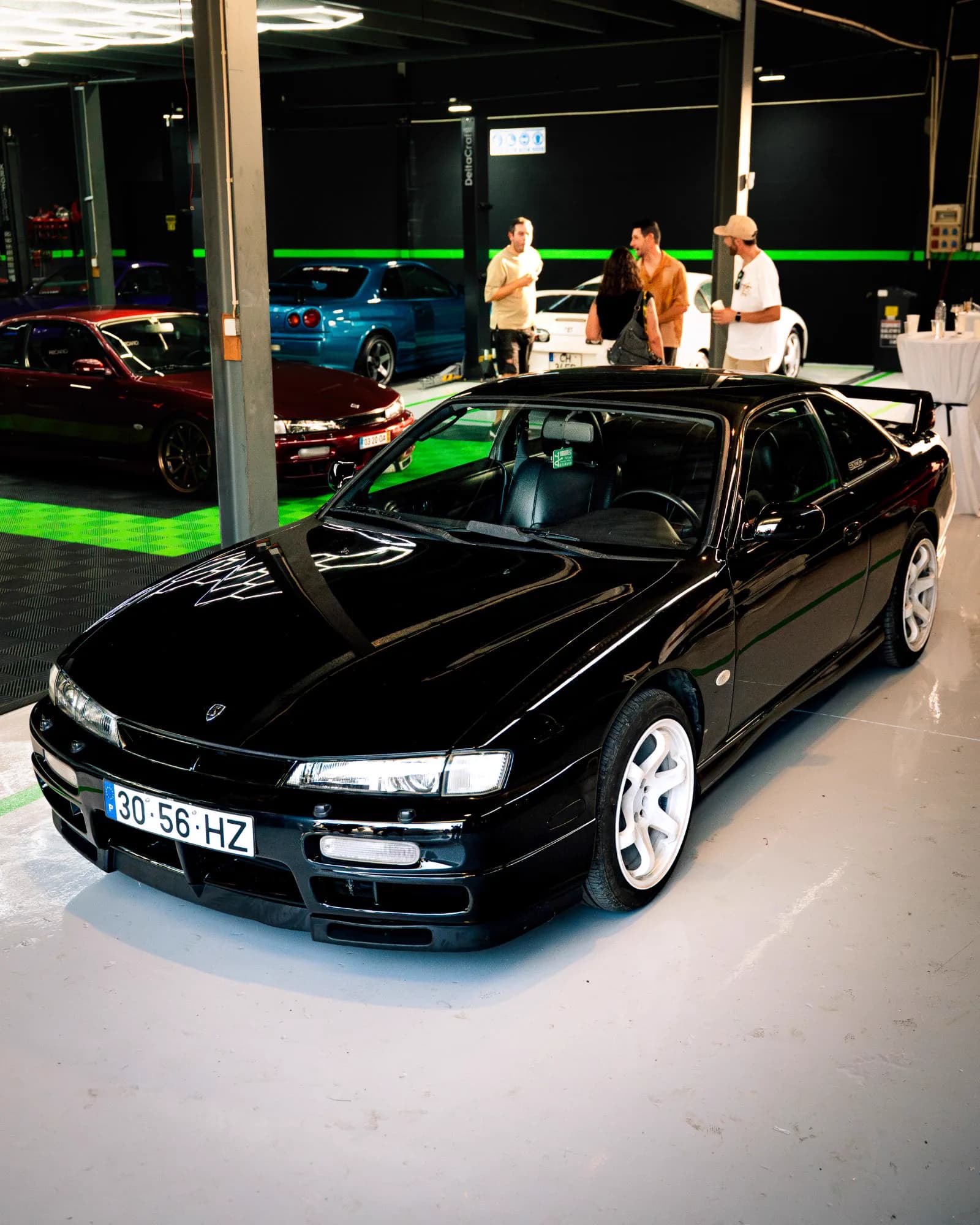 Nissan Silvia S14 preto com jantes brancas, com visitantes e outros carros ao fundo