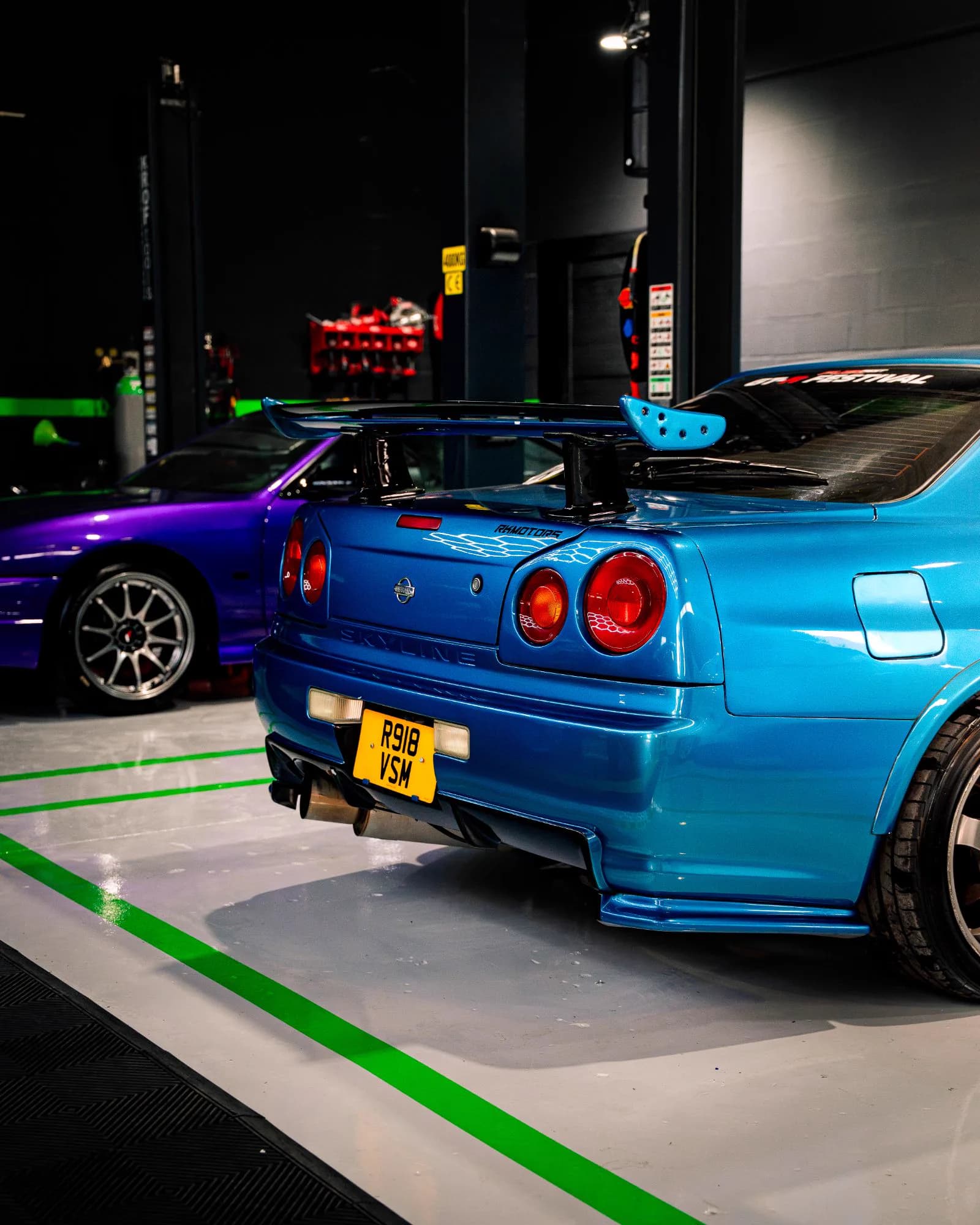 Traseira de um Nissan Skyline R34 azul com asa traseira, ao lado de um S14 roxo
