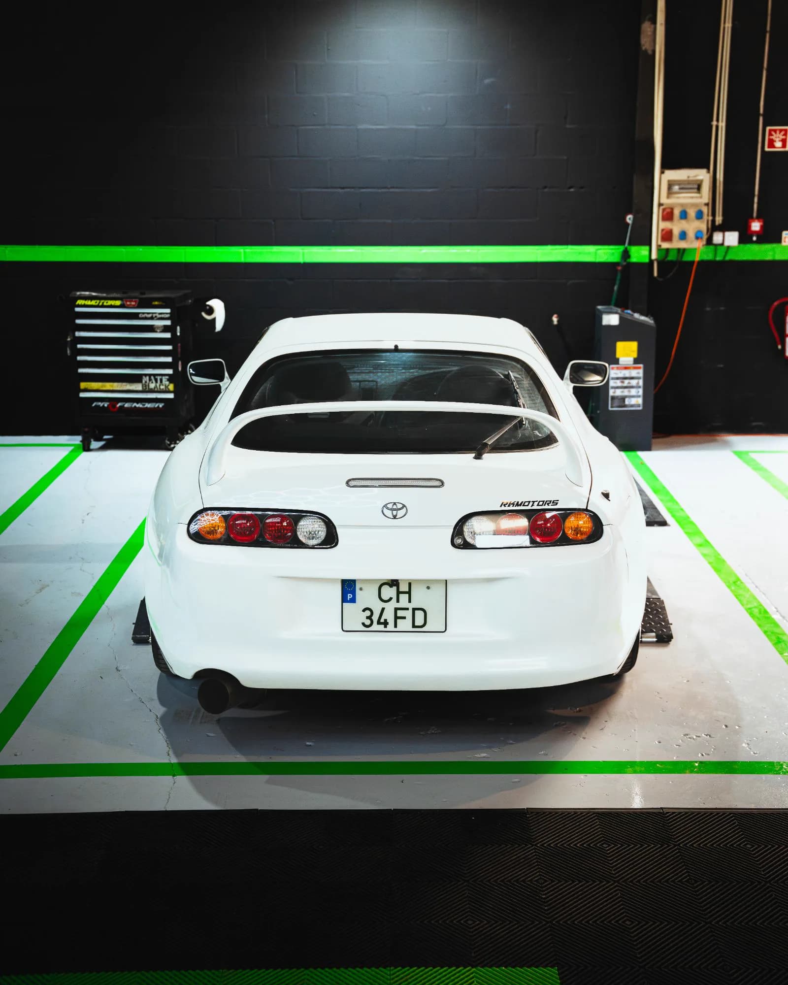 Traseira de um Toyota Supra branco estacionado entre as linhas verdes da oficina
