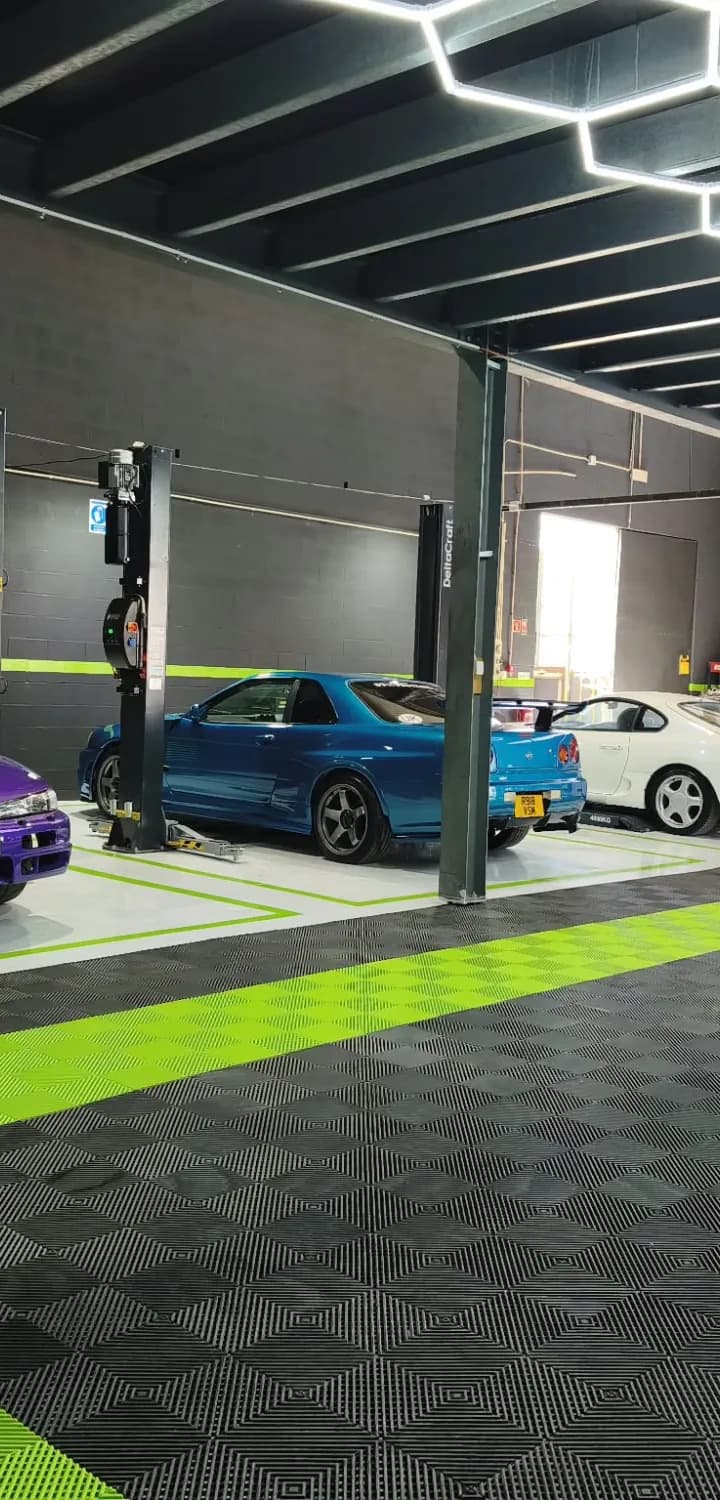 Interior da oficina com teto de luzes hexagonais e automóveis japoneses alinhados nos elevadores